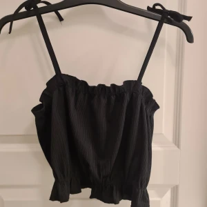 Svart ribbad linnetopp från H&M - Säljer en svart ribbad linnetopp från H&M med justerbara axelband som knyts. Toppen har en elastisk kant upptill och nertill för en bekväm passform. Perfekt till sommaren. Oanvänd med prislapp på.