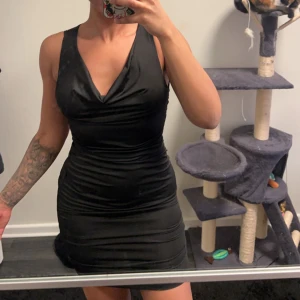 Svart tight klänning - Snygg svart klänning med v-ringad hals och tight passform. Perfekt för en kväll ute. Klänningen är ärmlös och har en kort längd som framhäver figuren.