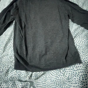 Grå tröja från 157 - Säljer en stilren grå tröja från 157. Tröjan har långa ärmar och är tillverkad i ett mjukt material som passar perfekt för kyligare dagar. Den har en enkel design med ribbade kanter vid ärmslut och nederkant.