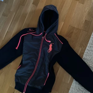 Svart vindjacka/kofta - Supercool sommarjacka/kofta! Ser ut som en vest med kofta under. Den är perfekt att ha under sommaren eller som träningsjacka. Den är använd men i fint skick förutom att drag grejen på dragkedjan gått av men den går fortfarande att stänga och öppna utan problem, samt att ”trådarna” är lite slitna (se bild 3).                              Jackan/koftan är i storlek XL men den är som en storlek S/M då den är liten i storlek.