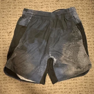 Mönstrade träningsshorts från Adidas - Snygga träningsshorts från Adidas med ett unikt mönster i svart och blått. De har en elastisk midja för extra komfort och är perfekta för intensiva träningspass. Materialet är lätt och andas bra.