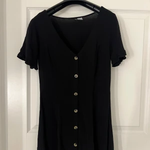 Svart klänning  - Snygg svart klänning från H&M Divided med knappar framtill v-ringad design som ger en stilren look.💗💗