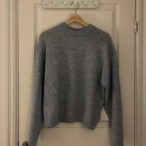 Ljusgrå stickad tröja - Säljer en ljusgrå stickad tröja med rund hals och långa ärmar. Perfekt för kyligare dagar och ger en mysig känsla. Tröjan har ribbade muddar vid ärmslut och nederkant.