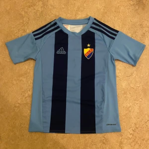 Blå djurgården fotbollströja från Adidas 140 - Snygg djurgårdens fotbollströja från Adidas i ljusblått och mörkblått med DIF-märket på bröstet. Tröjan har korta ärmar. Perfect för fotbollsfans som vill visa sitt stöd.