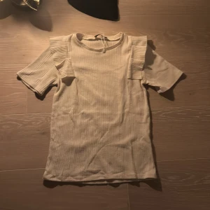 🎀vit ribbad topp med volangdetaljer🎀 - Säljer en stilren beige ribbad topp med korta ärmar och volangdetaljer på axlarna. 