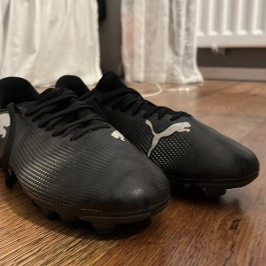Svarta fotbollsskor från Puma - Snygga svarta fotbollsskor från Puma med vit logga på sidan. Skorna har snörning och är designade för att ge bra grepp på planen. Perfekta för fotbollsträning och matcher.
