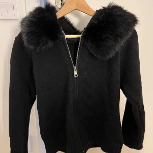 Svart stickad jacka med fuskpäls - HELT NY! Snygg svart stickad jacka med dragkedja och huva dekorerad med fuskpäls. Pris kan diskuteras 