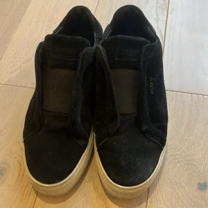 Svarta sneakers från Axel Arigato - Snygga svarta sneakers från Axel Arigato i mocka med en stilren design. Skorna har en vit sula och är utan snörning för en smidig påtagning. Perfekta för en avslappnad stil. allt og följer med sko påse klister märket och plastpåsarna till skorna inklusive pappret inuti skorna, storleken är 42 men passar också 43 så hör av dig om du har funderingar 👍