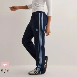 Mörkblå byxor från Adidas - Lågmidjade och jätte snygg passform. Snygga mörkblå byxor från Adidas med de klassiska tre ränderna i ljusblått längs sidorna. Byxorna har en elastisk midja och en avslappnad passform, perfekt för träning, skolan eller en avslappnad dag. Adidas-loggan är broderad på framsidan. Från Nelly, skriv om du har frågor( priset kan sänkas!!!)