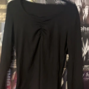 Svart långärmad topp - Säljer en stilren svart långärmad topp med rynkdetalj vid halsringningen. Perfekt för en enkel och elegant look. Passar bra till både jeans och kjol. Vet inte vart den är från.