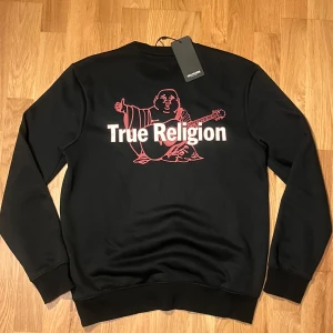 Svart sweatshirt från True Religion - Säljer en svart sweatshirt från True Religion med stora trycket på baksidan, knappt använd och köpt i usa✅🔥👌🏼                                               Pris kan diskuteras vid snabb affär👌🏼.                     Nypris 1200