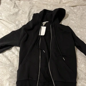 Svart hoodie från H&M - Säljer en svart hoodie från H&M i storlek XS. Den har en dragkedja framtill och en praktisk huva med snörning. Perfekt för en avslappnad stil. 🖤