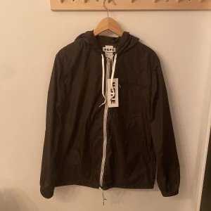 Windbreaker från Hope - Säljer en helt ny mörk khaki vindjacka från Hope! Jackan har en dragkedja framtill och en justerbar huva med snörning. Perfekt för blåsiga dagar och är allmänt chill ❤️sjukt bra pris, över 55% rea så passa på!