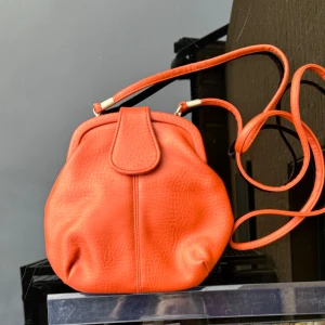 Orange axelväska i syntet - Ny Orange axelväska i syntet. Den har en enkel och stilren design med en lååång axelrem. Väskan stängs med en knapp och insidan har ett snyggt mönster. Mått -se bild med linjal. Hämtas på Hägerstensåsen eller ök 🧡🍑🟠🎃