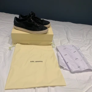 Svarta sneakers från Axel Arigato - Säljer ett par snygga svarta sneakers från Axel Arigato. De är i mocka och har en stilren design. Skorna är i bra skick och kommer med originalförpackning och dustbag. Skick 7/10, uk 8 / storlek 42/43,kan gå ner i pris vid snabbafär🍾