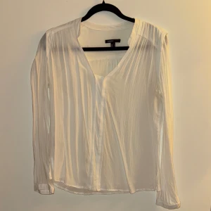 Vit blus från Mango - Säljer en elegant vit blus från Mango i storlek L. Blusen har långa ärmar och en lätt v-ringad design. Materialet är mjukt och ger ett luftigt intryck, perfekt för både vardag och fest. Den har en klassisk och tidlös stil som passar till många olika outfits.