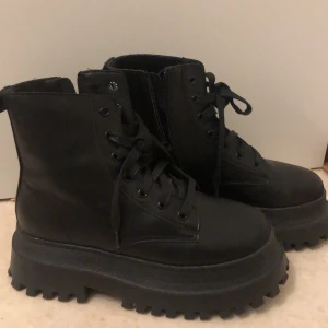 Svarta kängor med platåsula - Säljer ett par svarta kängor med rejäl platåsula och snörning. De är perfekta för höst och vinter med sin robusta design. Kängorna har en högre skaft och är gjorda i syntetmaterial, vilket gör dem både stiliga och praktiska och är knappt använda.