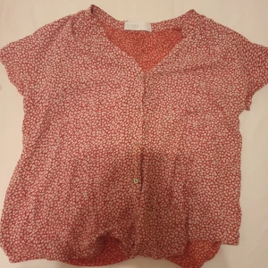 Röd blus - En röd blus med vitt blommönster. Blusen har en knappslå i fram och korta ärmar. Super fin säljs för 50 