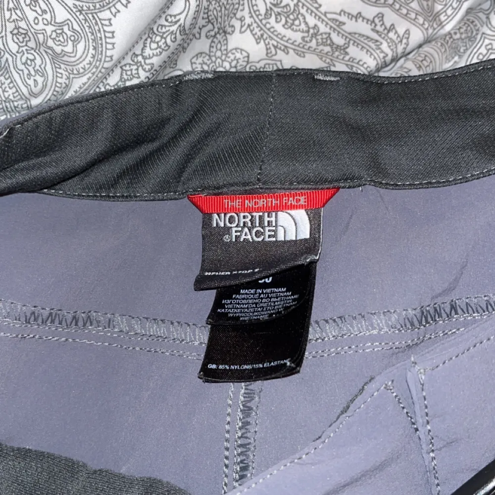 Säljer ett par grå shorts från The North Face i storlek M. De har en cool grön dragkedja på fickan och är perfekta för utomhusaktiviteter. Materialet känns slitstarkt och bekvämt, perfekt för sommarens äventyr. Passformen är loose, vilket gör dem sköna att röra sig i.. Shorts.