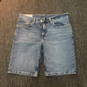 Säljer ett par klassiska blå jeansshorts från H&M i storlek 32. De har en regular fit och är perfekta för sommaren. Shortsen har fem fickor och stängs med en knapp och dragkedja. De är i bra skick och redo för nya äventyr!