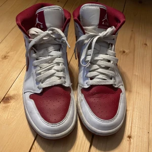 Nike Air Jordans i vitt och rött - Säljer ett par klassiska Nike Air Jordans i vitt och rött. Skorna har snörning och är i bra skick med några tecken på användning. Perfekta för både vardag och sportiga tillfällen. Storlek är inte specificerad, men de ser ut att passa en normal passform.