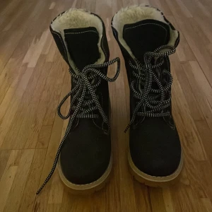 Svarta vinterstövlar med foder - Säljer ett par svarta vinterstövlar i mycket bra skick. De har en mysig vit foder inuti och snörning framtill. Perfekta för kalla vinterdagar med en robust sula för bra grepp. Passar både till vardags och lite mer äventyrliga utflykter.