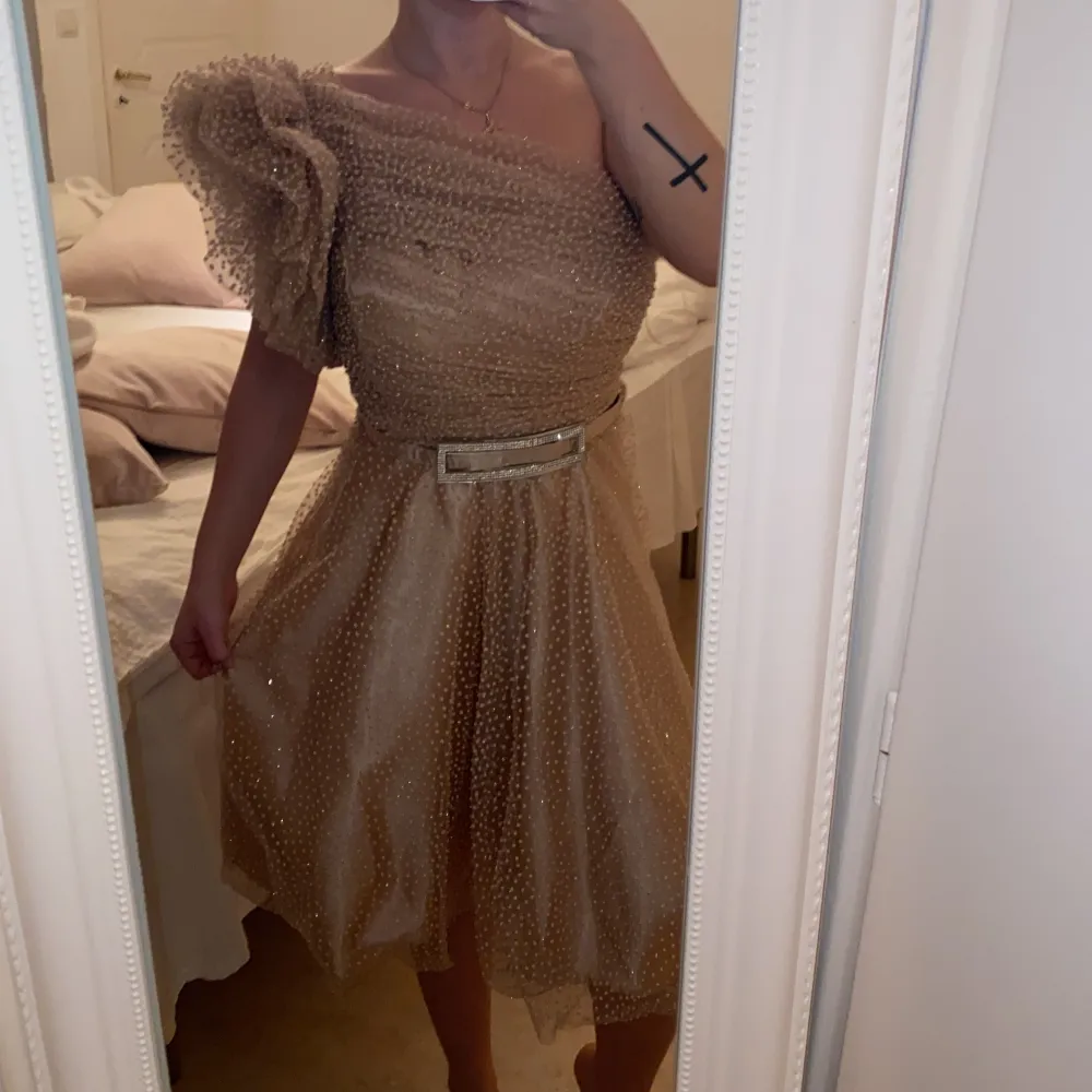 Säljer en superfin champagnefärgad klänning med glittrigt mönster. Den har en offshoulder-design med volangdetaljer och ett bälte i midjan. Perfekt för festliga tillfällen! 💫. Klänningar.