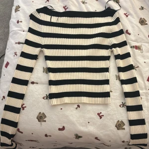 Randig ribbad tröja från H&M - Säljer en superfin randig tröja från H&M i svart och beige/vit. Den är ribbad och har en tight passform som sitter snyggt på kroppen. Väldigt stretchig och har slits vid ärmarna. Perfekt för både vardag och fest! 🖤🤍 Använd en gång!