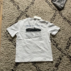 Vit t-shirt från Sayless - Säljer en snygg vit t-shirt från Sayless i nytt skick. Den har en cool porsche tryck på baksidan och en liten logga på framsidan. Nytt pris 400 mitt pris 200. Perfekt för en avslappnad stil eller en dag på stan. T-shirten är gjord i mjuk bomull och är väldigt skön.