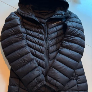 Svart dunjacka från Peak Performance - Säljer en svart dunjacka från Peak Performance i Nyskick. Den är enbart testad men missade reutunera den. Jackan har en snygg quiltad design med dragkedja och huva. Perfekt för kalla vinterdagar och höstpromenader. Den är både stilren och funktionell. Pris går att diskutera vid snabb och smidig affär!
