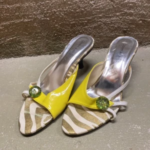 Zebramönstrade sandaler med gul detalj - Snygga sandaler med zebramönster och en iögonfallande gul detalj framtill. De har en liten klack och en glittrig dekoration som ger extra stil. Perfekta för sommarens fester eller en dag på stan. Skorna är i bra skick och redo för nya äventyr!