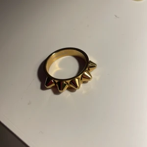 Guldfärgad ring med nitar - Snygg och edgy guldfärgad ring med coola nitar runtom. Perfekt för att ge din outfit en tuff touch. Ringen är i mycket bra skick och passar perfekt för både vardag och fest. passar bra på pekfingret