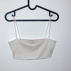 Vit axelbandslös tubtopp - Säljer en stilren vit tubtopp med smala axelband. Perfekt för sommardagar eller som ett basplagg i garderoben. Toppen är i ett mjukt och bekvämt material som passar till många olika outfits.