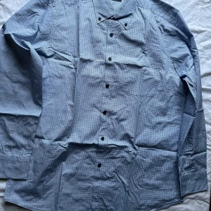 Blå mönstrad skjorta från Park Lane - Säljer en stilren blå skjorta från Park Lane med ett diskret mönster. Skjortan har långa ärmar och knappar framtill. Perfekt för både vardag och festliga tillfällen. Materialet känns bekvämt och passar bra till både jeans och kostymbyxor. Hör av dig vid intresse! 