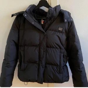 Svart dunjacka från Levi's - Säljer en svart dunjacka från Levi's i storlek S. Jackan är varm och vattenavvisande, perfekt för kalla och blöta dagar. Den har en huva och stängs med dragkedja och knappar. Passar perfekt för vintern! 🖤