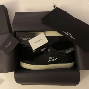 Saint Laurent Svarta sneakers - Säljer ett par snygga svarta sneakers från Saint Laurent i nytt skick. Skorna har en stilren design med vit sula och Saint Laurent-logga på sidan. Perfekta för både vardag och fest! Kommer i originalförpackning med tillhörande dustbag och kort.