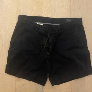 Svarta shorts från Polo Ralph Lauren - Säljer ett par snygga svarta shorts från Polo Ralph Lauren. De är i bra skick och har en klassisk design med dragkedja och knapp. Perfekta för sommaren eller våren. Tillverkade i ett bekvämt material som passar både till vardags och lite finare tillfällen.
