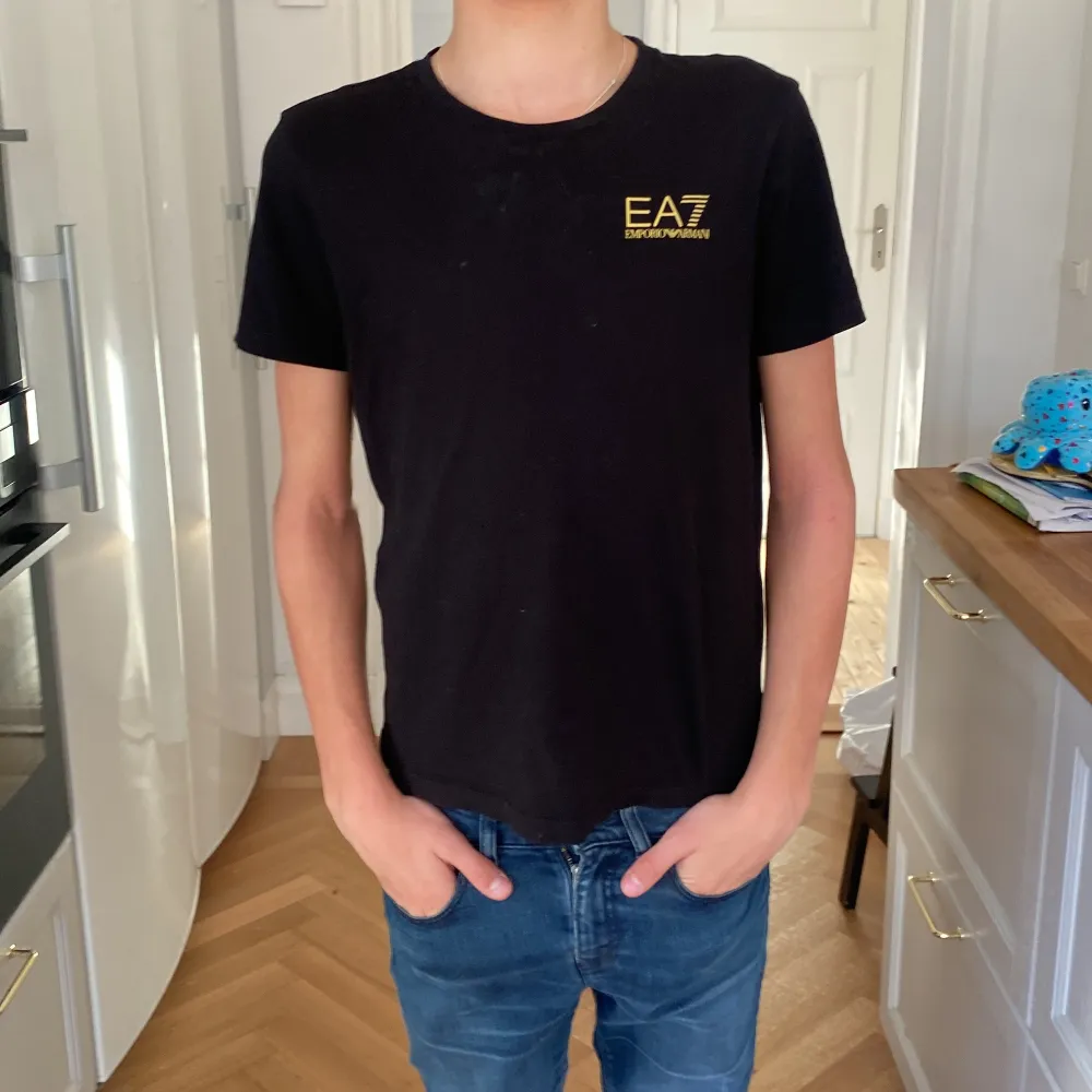 Säljer en svart t-shirt från Emporio Armani i bra skick. Den har en gul logga på bröstet och är gjord av bomull. Perfekt för vardagsbruk eller en avslappnad utekväll. Passar bra till jeans eller shorts! Säljer pga att tröjan är för liten för mig. Storleken är EU 14A USA 14Y 160cm pris kan diskuteras! . T-shirts.