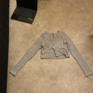 Grå ribbad croppad tröja från Shein - Säljer en superfin grå ribbad tröja från Shein i storlek M. Den är croppad och har en omlott-design som ger en snygg look. Perfekt för både vardag och fest! Tröjan är i mycket bra skick och redo för en ny ägare. 💫