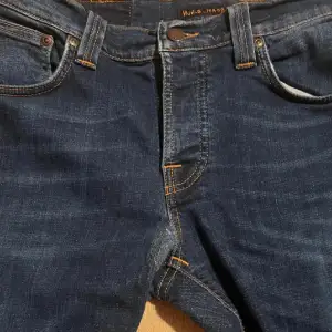 Säljer ett par snygga mörkblå jeans från Nudie Jeans i modellen Grim Tim. Perfekta för både vardag och fest med sin klassiska stil och bekväma passform. Har ett igensytt hål men syms inte så tydligt.