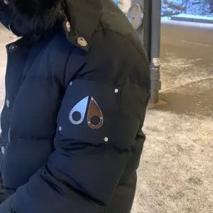 Säljer en svart pufferjacka från Moose Knuckles i mycket bra skick. Jackan har en stilren design med en snygg logga på ärmen och knappar framtill. Perfekt för kalla vinterdagar med sin varma och quiltade insida. Passar både till vardags och festliga tillfällen.