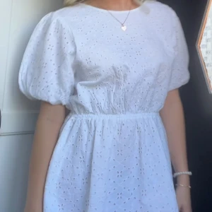 Vit klänning med öppen rygg och knyt - Säljer en superfin vit klänning med puffiga kortärmar och ett vackert broderat mönster. Den har en öppen rygg med knytband som ger en söt och romantisk look. Perfekt för sommarens alla fester eller en mysig midsommar eller student. Klänningen är i mycket bra skick och passar perfekt för en solig dag! Storlek 170 men passar som S!
