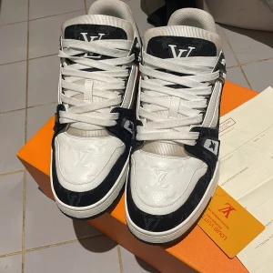 LV Trainers ( svartvit ) - Säljer ett par snygga svartvita Louis Vuitton sneakers i nytt skick. De har en stilren design med LV-loggan på tungan och sidan. Skorna är i skinn och har en bekväm passform med snörning. Perfekta för både vardag och fest! Kvitto och allt finns.