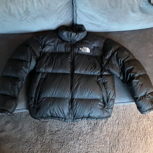 Svart pufferjacka från The North Face - Säljer en snygg och varm svart pufferjacka från The North Face, modell Retro Nuptse.  Jackan är använd en vinter och har två små lagningar men är i väldigt bra skick. Nypris är ca 3000 kr.