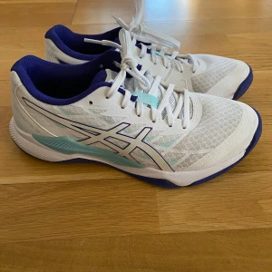 Vita och blå Asics sneakers - Säljer ett par snygga Asics sneakers i vitt och blått. De har en sportig design med snörning och en slitstark sula. Perfekta för träning eller vardagsbruk. Skorna är i mycket bra skick och redo för nya äventyr!