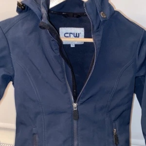Mörkblå stalljacka från CRW - Säljer en mörkblå stall jacka från CRW i bra skick. Den har en dragkedja framtill och praktiska fickor med dragkedjor. Perfekt för stallet med sin stilrena design och bekväma passform. Jackan är långärmad och gjord i ett slitstarkt material.