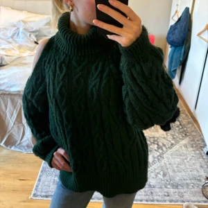 Mörkgrön stickad tröja med polokrage - Säljer en supermysig mörkgrön stickad tröja med polokrage. Den har en unik offshoulder-design som ger en cool touch. Perfekt för höst och vinter när du vill hålla dig varm och stilren. Tröjan är oversized och har långa ärmar med ribbade muddar. Passar perfekt till jeans eller leggings!