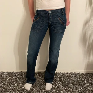 Mörkblå jeans från Diesel - Säljer ett par snygga mörkblå jeans från Diesel i bra skick. De har coola detaljer och en unik design på fickorna. Perfekta för både vardag och fest! Passar bra till en casual look eller när du vill klä upp dig lite extra.