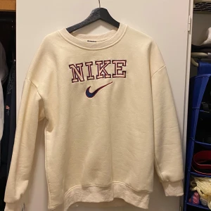 Beige sweatshirt från Nike - Säljer en superbekväm beige sweatshirt från Nike i storlek XL. Den har ett stort Nike-logotyptryck i rött och blått på framsidan. Perfekt för en avslappnad stil och passar till alla årstider. Tröjan är i mycket bra skick och redo för nya äventyr!