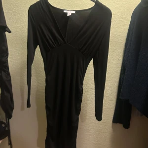 Svart klänning från Amisu - Snygg svart klänning från Amisu i storlek EU 34. Den har en v-ringad design och långa ärmar, perfekt för en kväll ute eller en fest. Klänningen är tight och framhäver figuren på ett elegant sätt. Tillverkad i Turkiet.